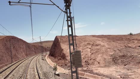 Railway-tracks-and-power-line-in-arid-land,-Morocco-by-train-journey