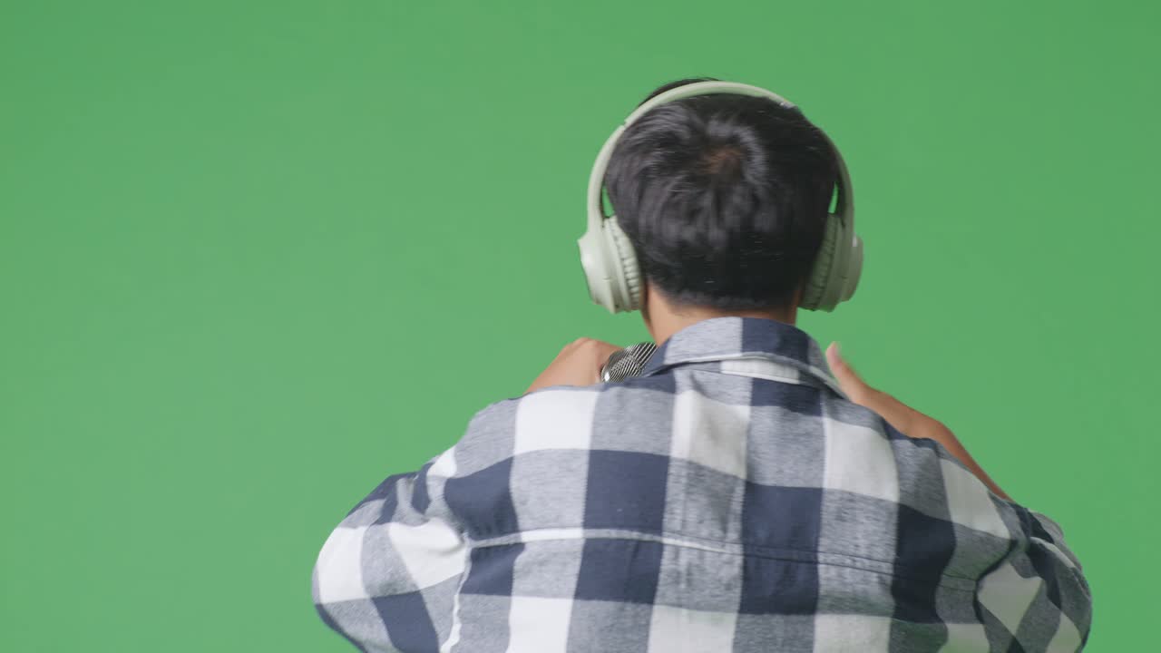 녹색 스크린 배경에서 마이크를 들고 하는 젊은 아시아 십대 소년의 근접 뒷면