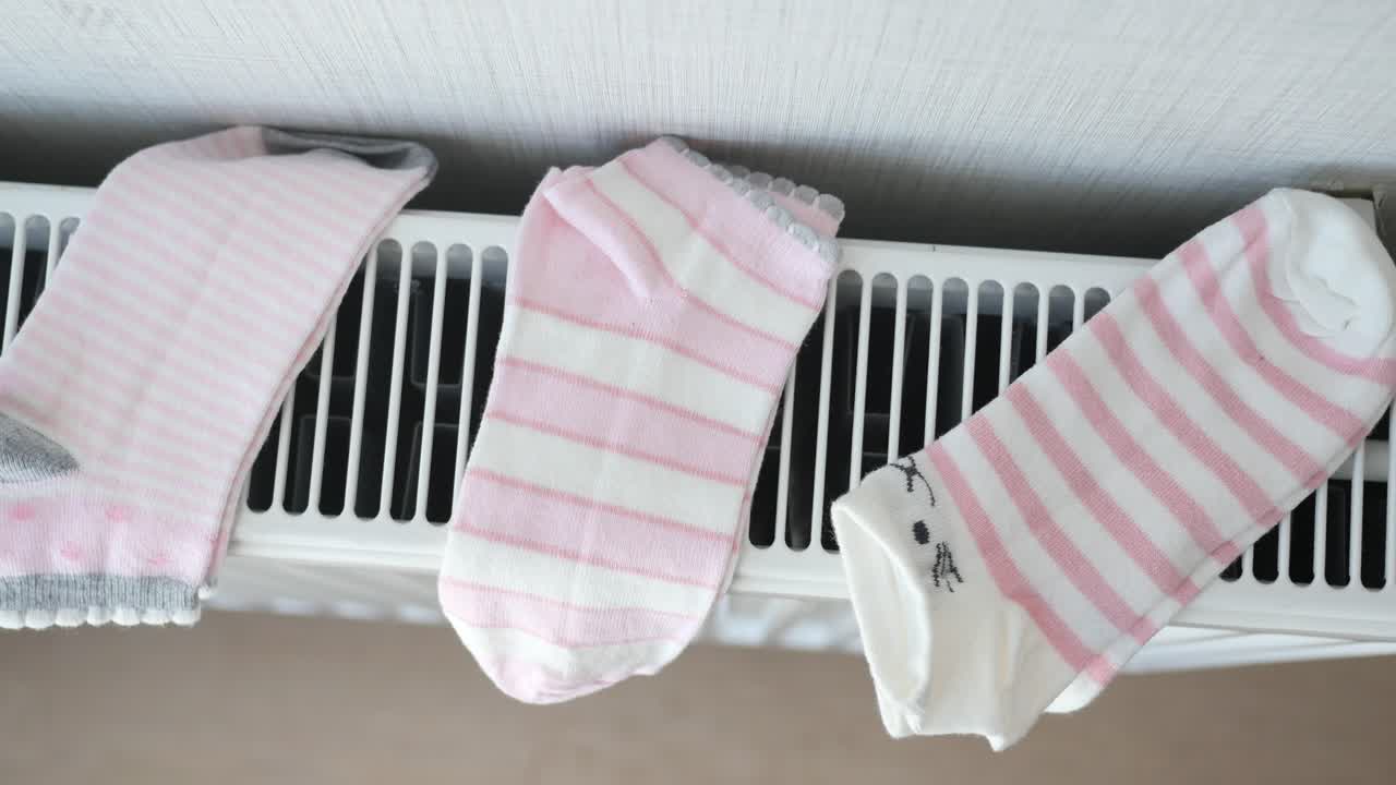 Lyserøde og hvidstribede sokker tørrer på radiator