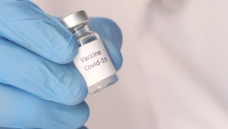 close-up of a hand in a blue glove holding a covid-19 vaccine vial