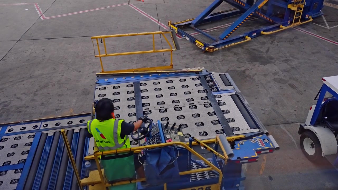 Chicago, EE. UU., 9 de mayo de 2026: Un trabajador de tierra opera un cargador de carga en la plataforma del aeropuerto de Chicago. Una vista elevada muestra una plataforma de rodillos azul, un vehículo de servicio y hormigón marcado junto al operador