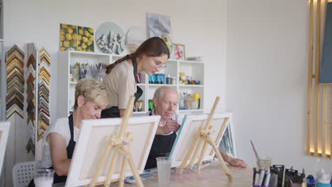 side view of a happy senior people smiling while drawing as a recreational activity or therapy in paint class together with the group of retired women and men