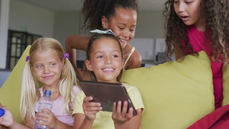 Video-of-diverse-girls-sitting-at-school-common-room-with-tablet,-talking-and-laughing