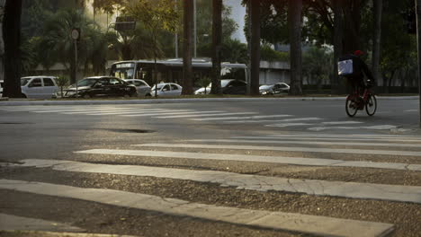 Bike-cyclist-app-deliverer-crossing-the-street-in-a-big-city-by-the-crosswalk-under-the-sunset-golden-light-filmed-in-slow-motion-in-4K-high-definition