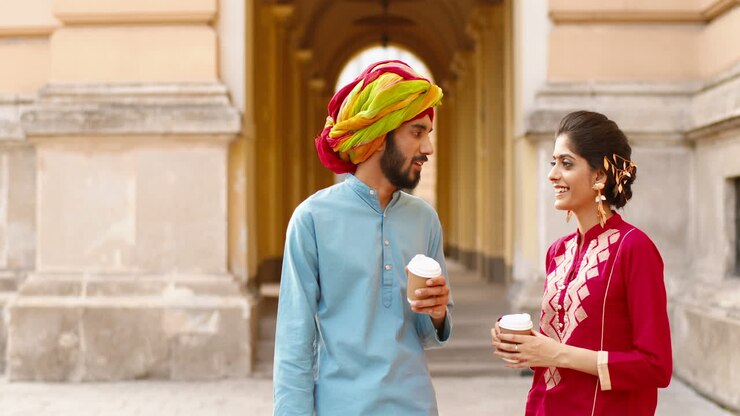 Hindu woman with dot on forehead and man in turban standing outdoors, talking and drinking coffe or tea. Resting. Male and female sipping drink and spending time together.