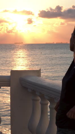 woman watching the sunset over the ocean from a balcony