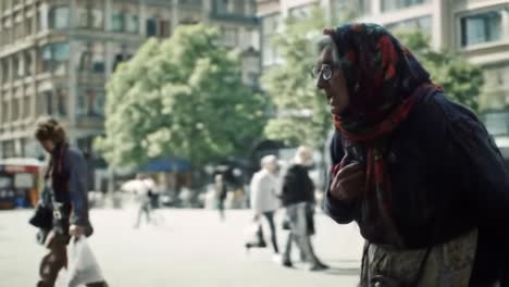 in a vibrant city market, an elderly woman wearing a scarf walks purposefully among busy pedestrians, showcasing daily life in an urban setting during the afternoon sun.