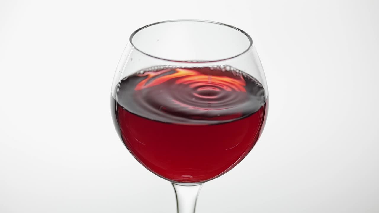 빨간 포도주와 함께 유리잔에 떨어지는 한 방울의 가까운.  바탕에 장미 포도주