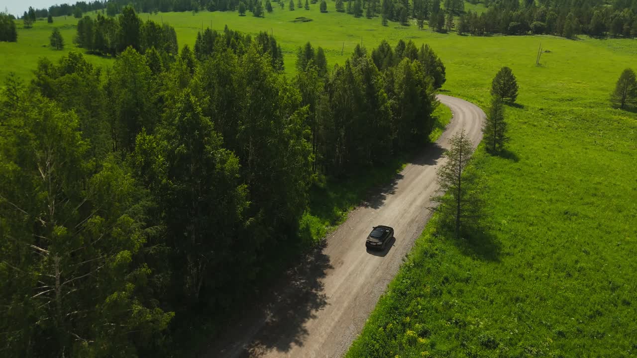 Letecký pohled na auto jedoucí po klikaté polní cestě zeleným lesem