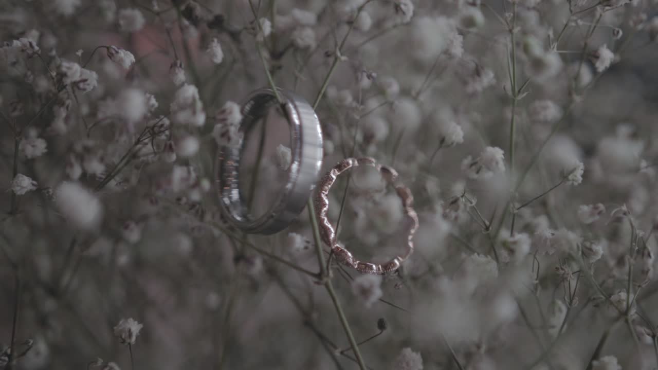 Dolly shot of diamond and gold wedding rings placed on a bed of baby's breath