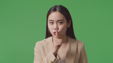 스튜디오의 녹색 스크린 배경에서 침 제스처를 보여주는 아시아 사업가의 클로즈업
