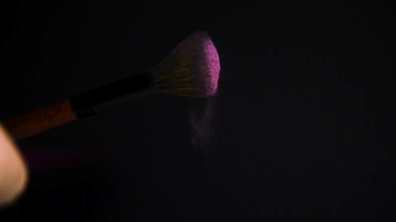 Slowmotion af en makeupbørste med lyserød pudder-eksplosion og spredning på sort baggrund