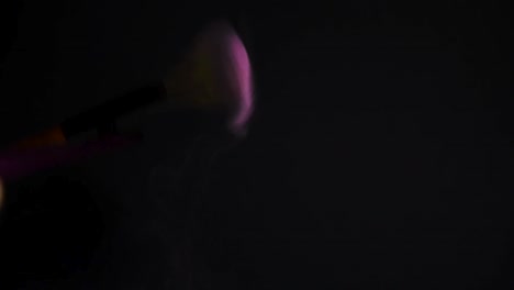 slow motion of a make up brush with pink powder explosion and burst on black background