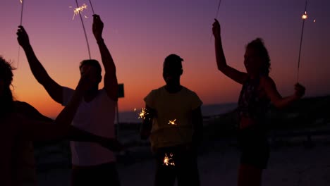 Amigos-Adultos-Jóvenes-Divirtiéndose-En-La-Playa-Por-La-Noche-Con-Bengalas-4k