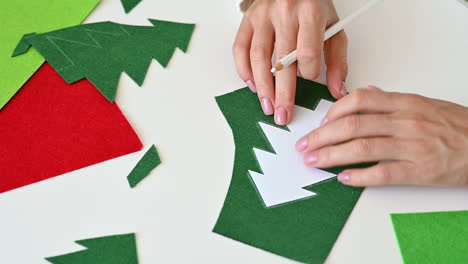 female hands cut out a christmas tree of green fabric with scissors using a template