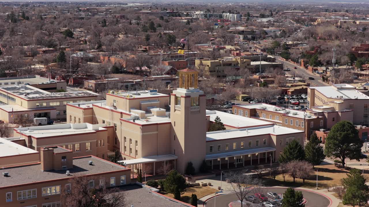 A smooth aerial orbit showcases the unique Southwestern architecture of the New Mexico State Capitol. This 4K perspective highlights the building's circular design and adobe-toned facade