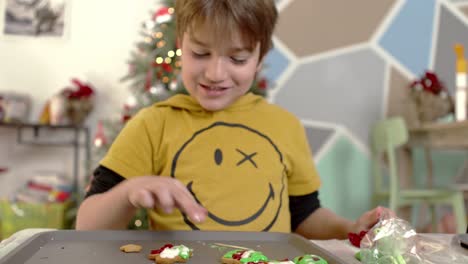 caucasian kid tasting sugar icing, preparing christmas homemade gingerbread cookies,christmas tree on the blurry background 4k