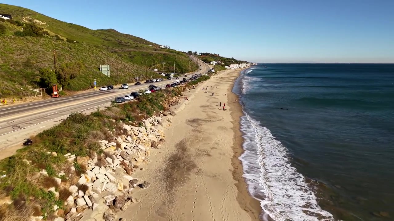 Onde dell'Oceano Pacifico si infrangono contro la costa rocciosa della California in dettaglio ravvicinato, con il potente moto ondoso che si rompe su una spiaggia sabbiosa costiera in una splendida giornata di sole e cielo sereno.