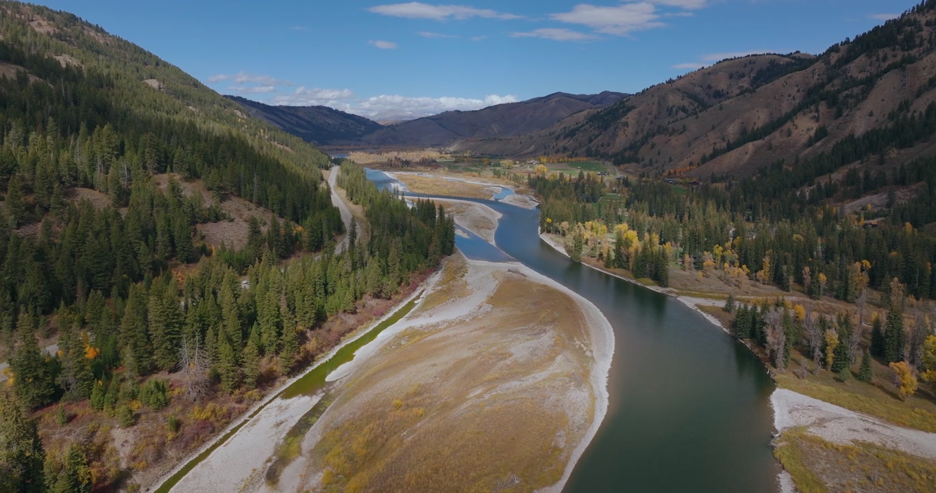 Aerial tracking left of winding river flowing through forested mountain valley in Wyoming