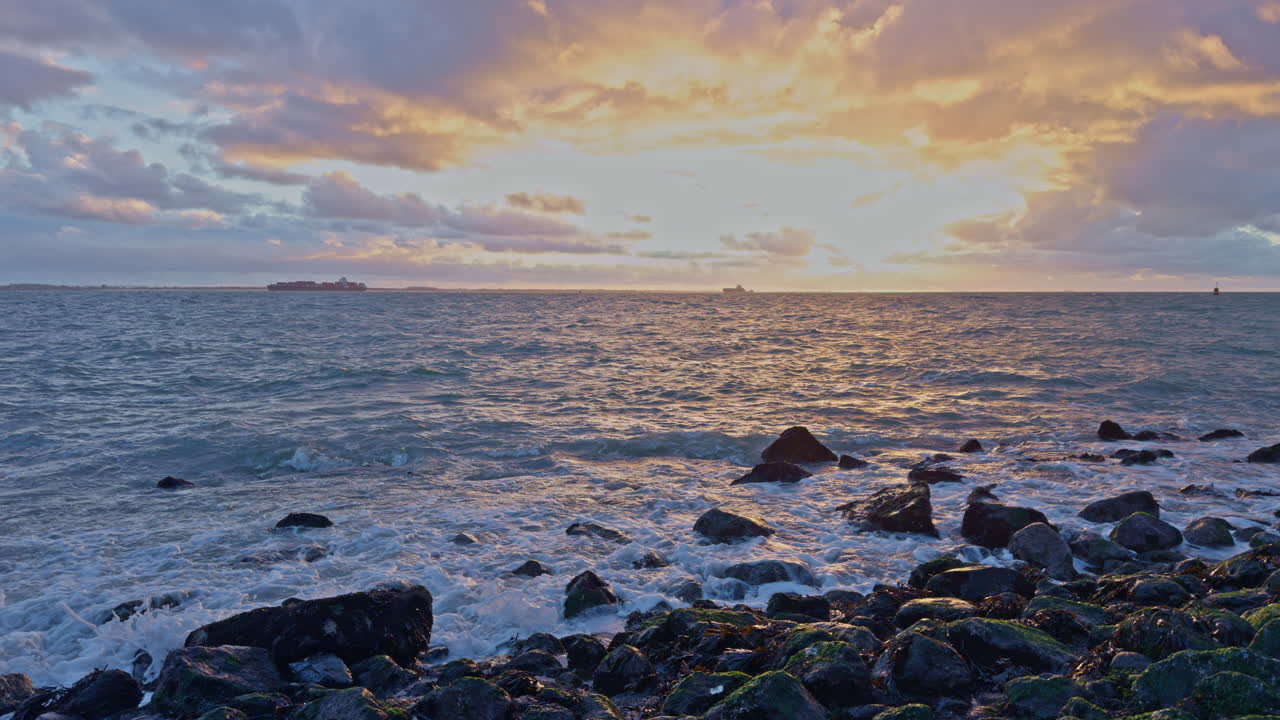 Atlantic ocean sea shore scenery view of water waves with reefs, clouds, sunlight and sunset with a ship boat ferry on the skyline horizon in the evening in North Europe, slow motion footage