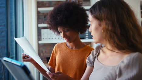 due colleghi d'affari femminili con tablet digitali e documenti che si incontrano insieme in ufficio