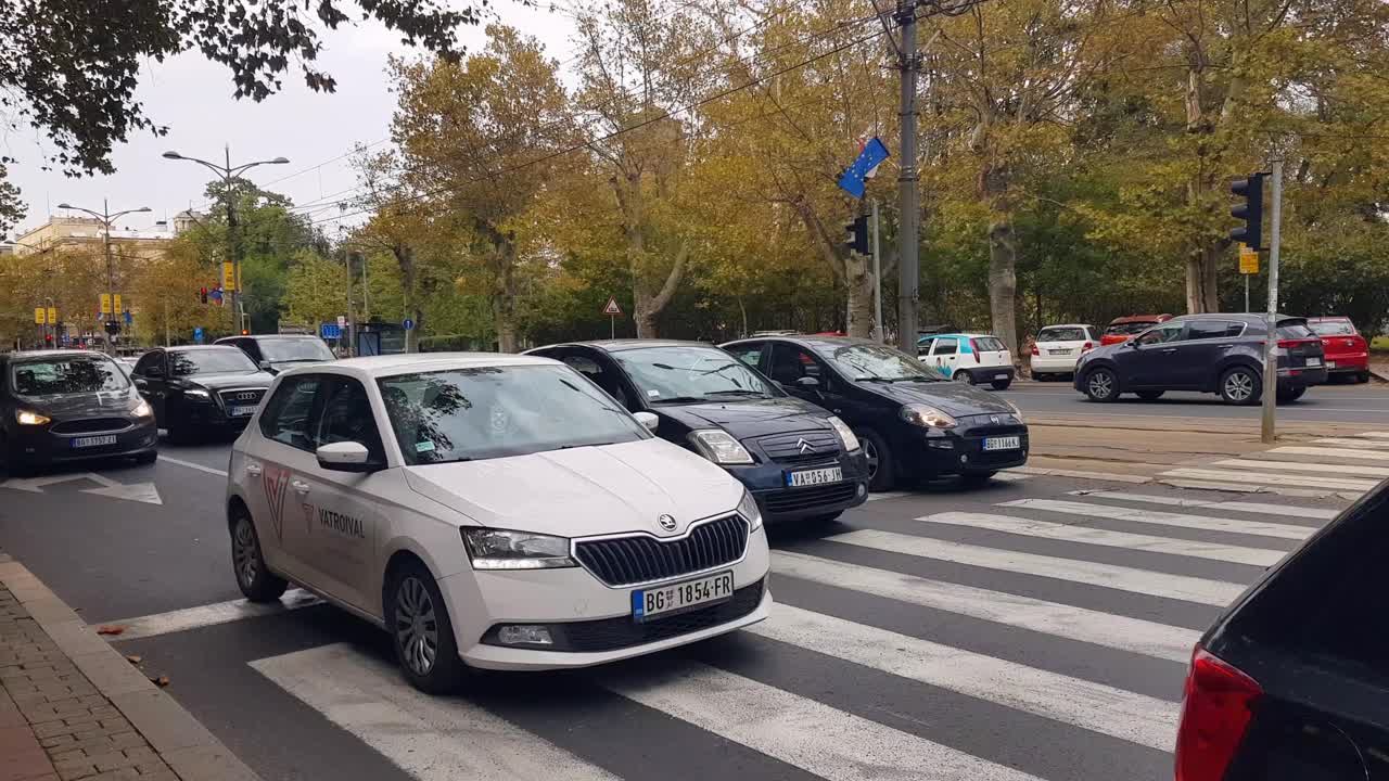Cars starting engines and driving off at intersection on an overcast spring day. Trees of Tasmajdan park in the background, Belgrade, Serbia