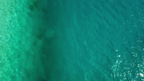 aerial, tilt up, drone shot, over a line separating turquoise, aqua menthe, lagoon water and darker teal colored ocean, revealing villas on the sea, on a sunny day, in maldives