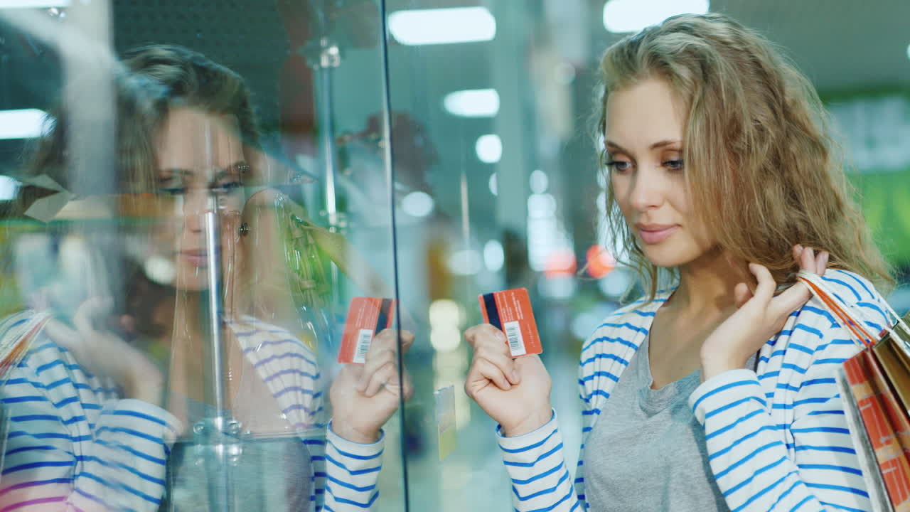 가게에 있는 유리 진열장을 보고 있는 매력적인 젊은 여성이 카드를 들고 있는 손