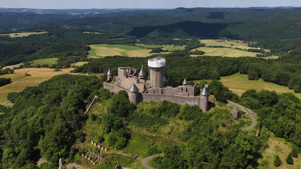 Nurburg castle, ruins of ancient castle on top of hill. Race track Nurburgring surrounding the monument. Aerial video