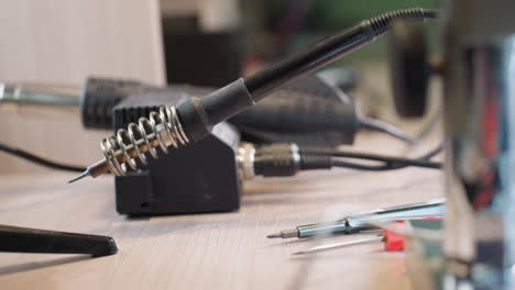 a close-up view of a soldering station with a soldering iron resting in its holder, surrounded by various electronic repair tools on a workbench