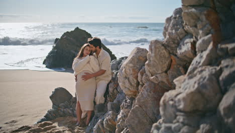 pregnant couple bonding beach near stone cliffs. man caressing big woman belly