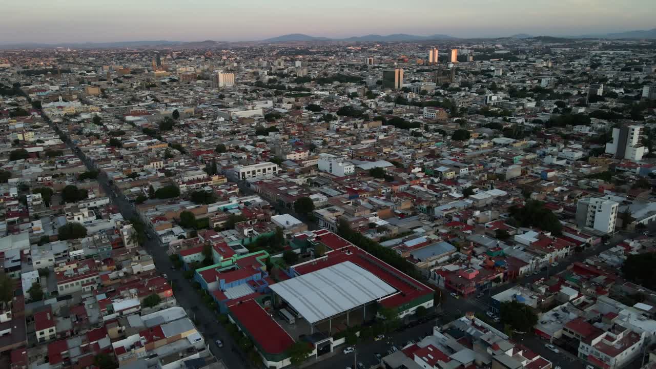 Recuo aéreo amplo mostrando toda a extensão da cidade de Guadalajara e um horizonte de colinas distantes após o pôr do sol. Filmado em 4K Apple ProRes 422