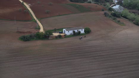 aerial view toward rural countryside with farm house and people horseback riding