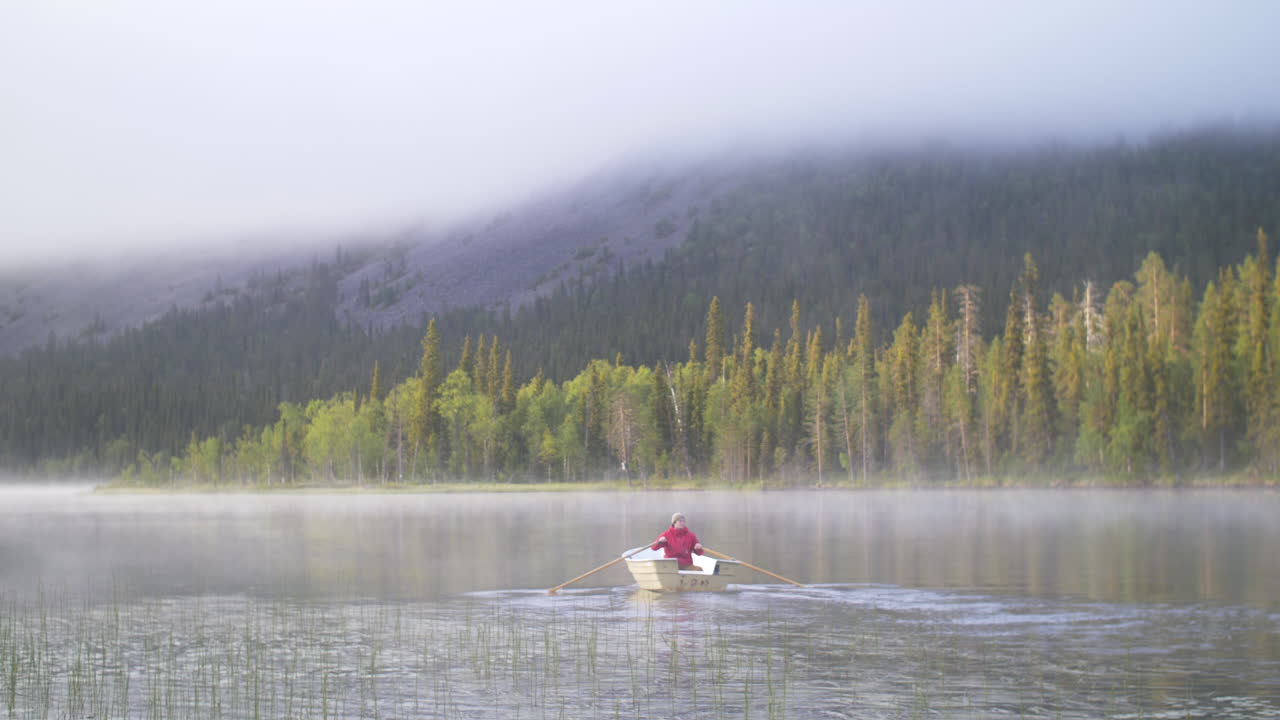 푸른 숲과 산을 배경으로 안개 낀 호수에서 작은 배를 노를 젓는 청년