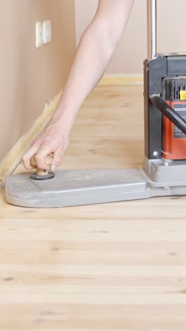 vertical - person operating edge sander along baseboard of wooden floor. floor refinishing works. closeup shot