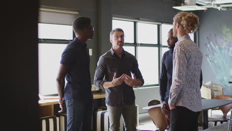 four male creatives stand having a discussion in their workplace, three quarter length, close up