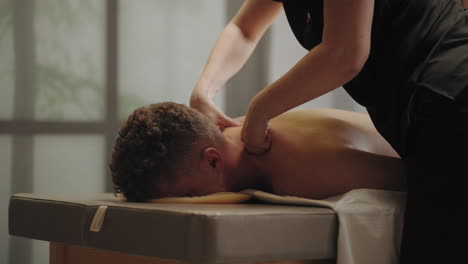 un hombre se relaja y disfruta de un masaje en un salón de spa. una masajista profesional está acariciando el cuello de un paciente masculino adulto.