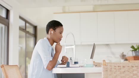 African-american-woman-sitting-at-table-wearing-earphones-and-using-laptop,-slow-motion