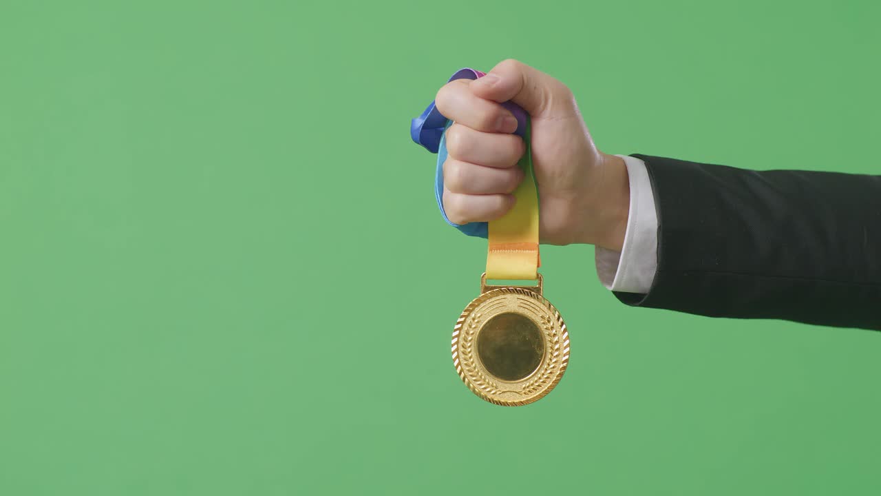 cerca de la mano del hombre de negocios sosteniendo una medalla de oro a su lado mostrando el premio como el primer ganador en el fondo de la pantalla verde en el estudio