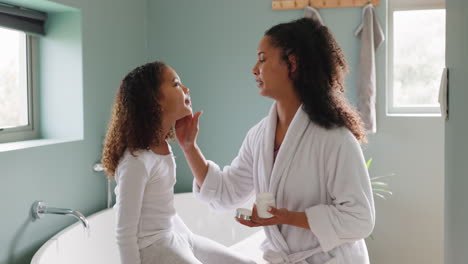 mother applying face cream to daughter in bathroom