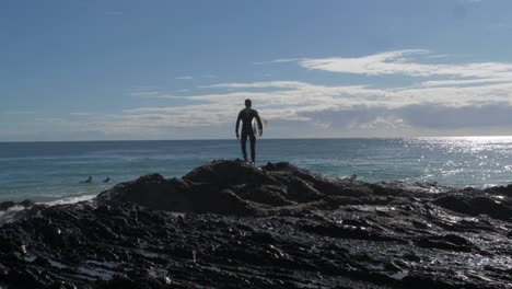 hombre con tabla de surf se encuentra en las rocas con olas salpicadas - surf en rocas de pargo - coolangatta, costa dorada, australia