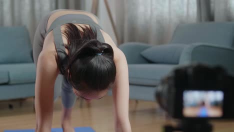 young asian trainer female in sports clothes speaking to camera and stretching while recording teaching exercise at home