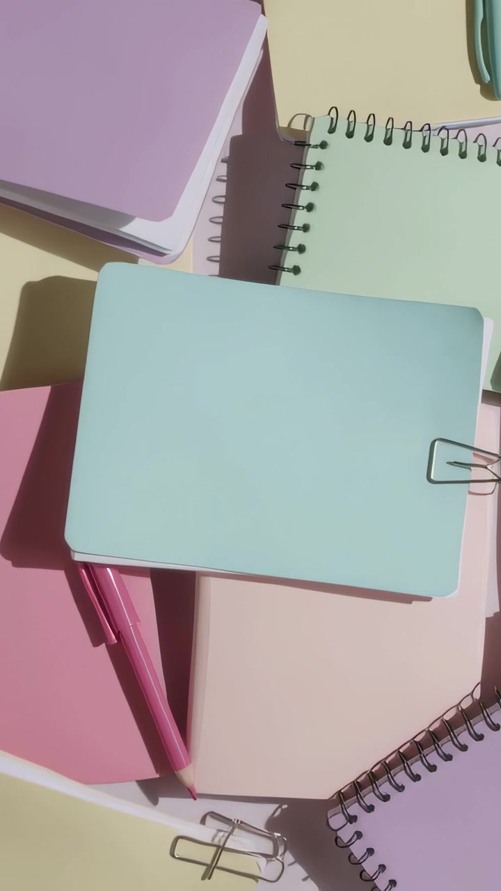 Video verticale: Telecamera che si inclina su un quaderno color menta su un tavolo giallo, documentando cancelleria pastello