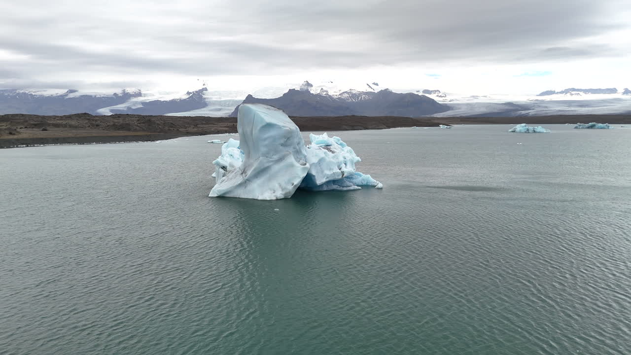 Aerial view of a massive iceberg floating in Jökulsárlón Glacier Lagoon, Iceland, highlighting the icy blue waters, surrounding glaciers, and serene Arctic scenery