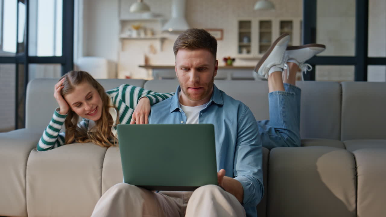 Serious man working laptop bored girlfriend leaning at sofa distracted husband