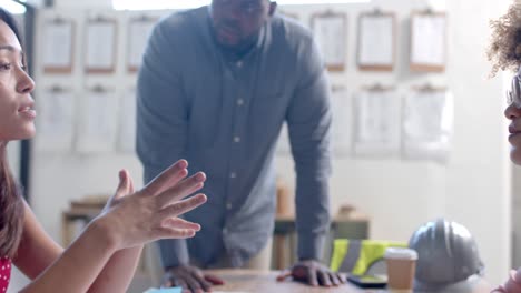 Happy diverse male and female architects discussing blueprints on table in office, slow motion