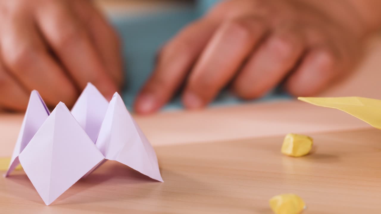 Primo piano di mani che piegano con cura un foglio di carta blu su un tavolo di legno per fare origami