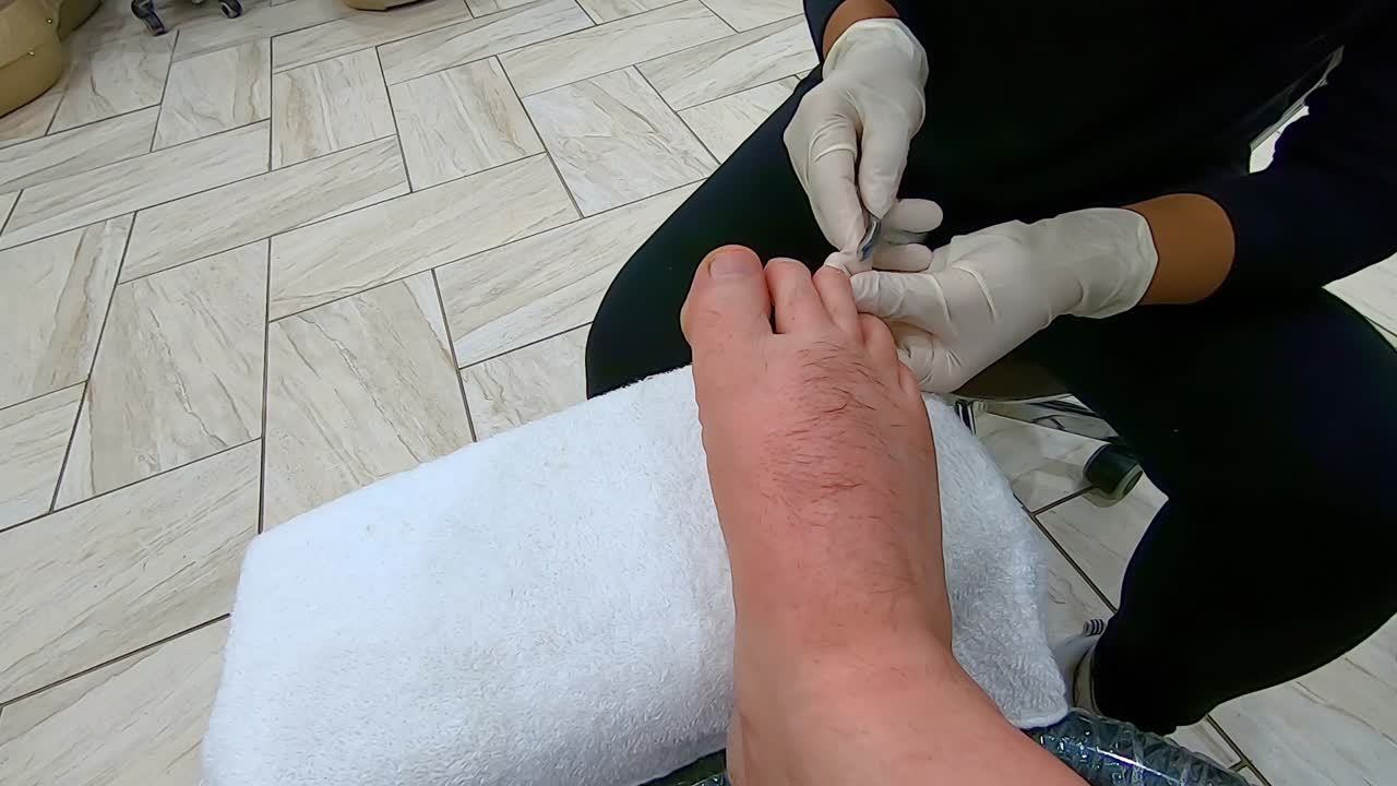 pedicurista profesional recorta las cutículas en el dedo medio derecho de un hombre usando pinzas para cutículas