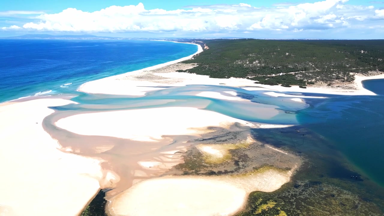 Laguna costiera e litorale sabbioso in Portogallo con acqua turchese, banchi di sabbia tidali, piccole imbarcazioni e paesaggio residenziale circostante, vedute aeree