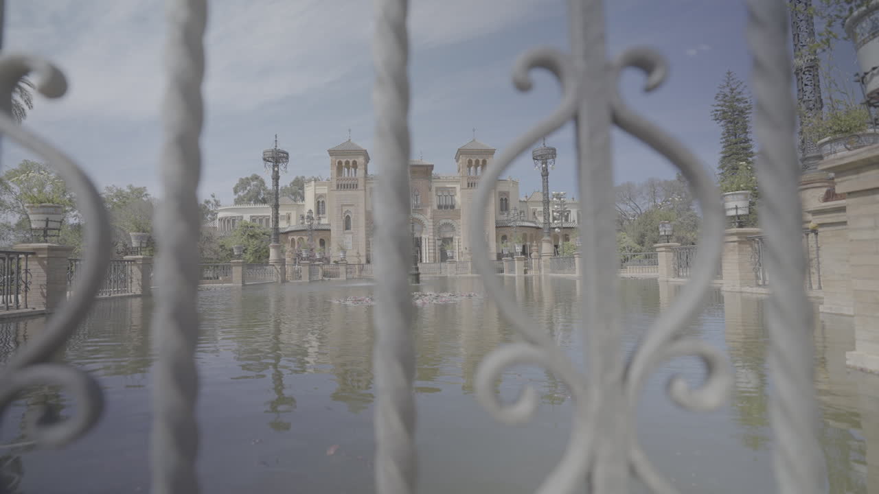 Building in the middle of Parque de Maria Luisa in Sevilla Spain on a sunny day in slow motion  viewed from behind a fence LOG
